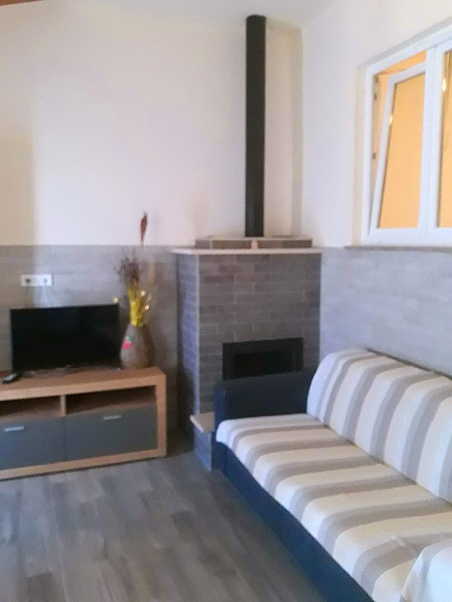 A living room with a sofa, a fireplace, a television on a stand, and a window with curtains.
