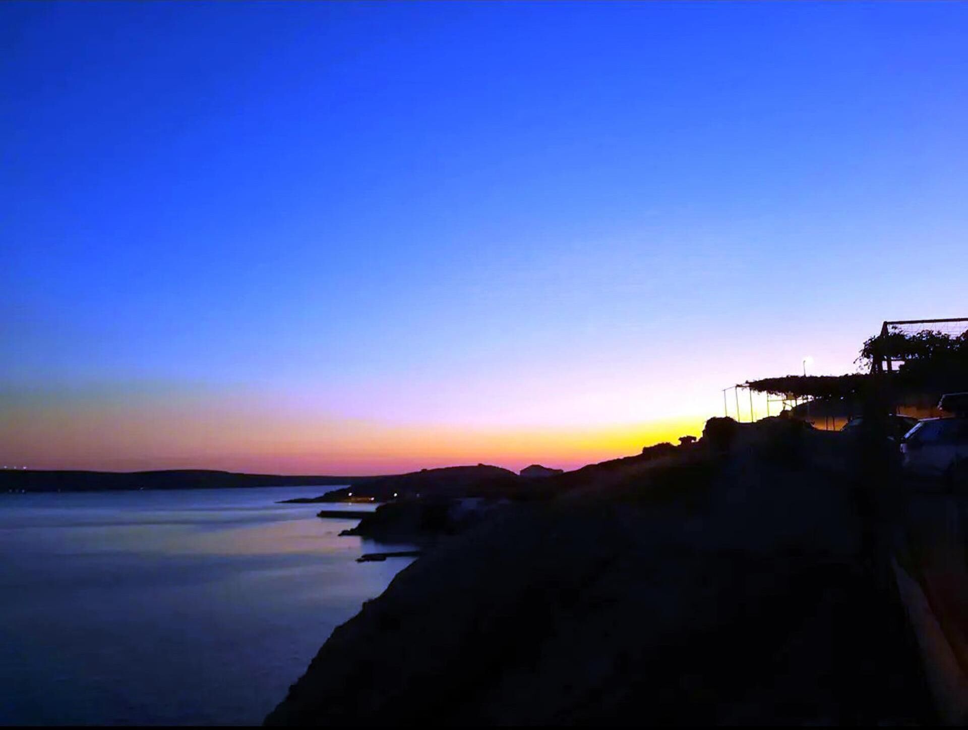 Vista de un atardecer costero con aguas tranquilas y terreno rocoso.