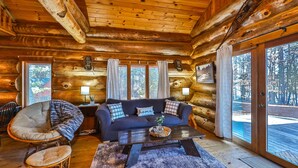 A log cabin interior with a dark blue sofa, a wicker chair, and a wooden coffee table. - Retreat at Blueberry (Osage)