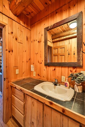 Ein Badezimmer in einer Holzhütte mit einem großen Spiegel, einem Waschbecken und einem Holfläschchen.