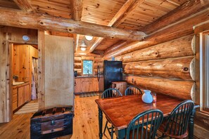 Ein Holzhütten-Interieur mit einem Holzespeisesaal, Stühlen, einem Kühlschrank und einem Spülbecken in der Küche.