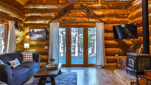 A log cabin interior with a sofa, armchair, television, and fireplace. - Retreat at Blueberry (Osage)