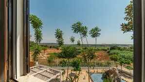 Une vue depuis un balcon donnant sur un jardin aménagé avec une piscine, des palmiers et une vue lointaine sur un pont.