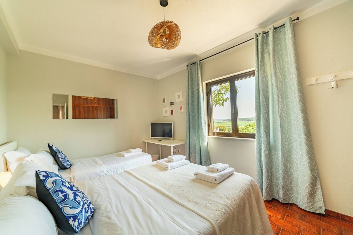 A hotel room with two beds, a TV, a desk, and a window with curtains.