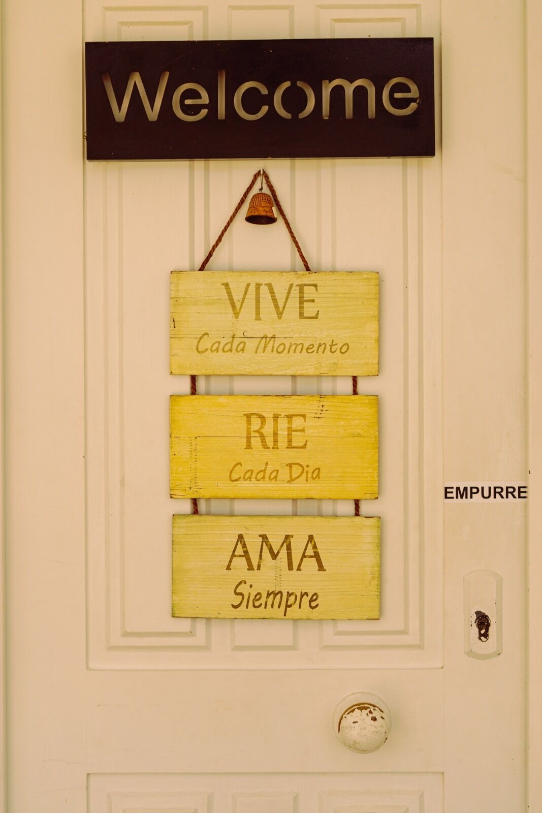 Una puerta con un letrero que dice 'Welcome' encima y tres letreros de madera abajo con frases motivacionales.