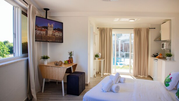 A hotel room with a bed, a desk, a television, and a balcony with curtains. - 4Ever Palace Design & Nature (Alcacer do Sal)