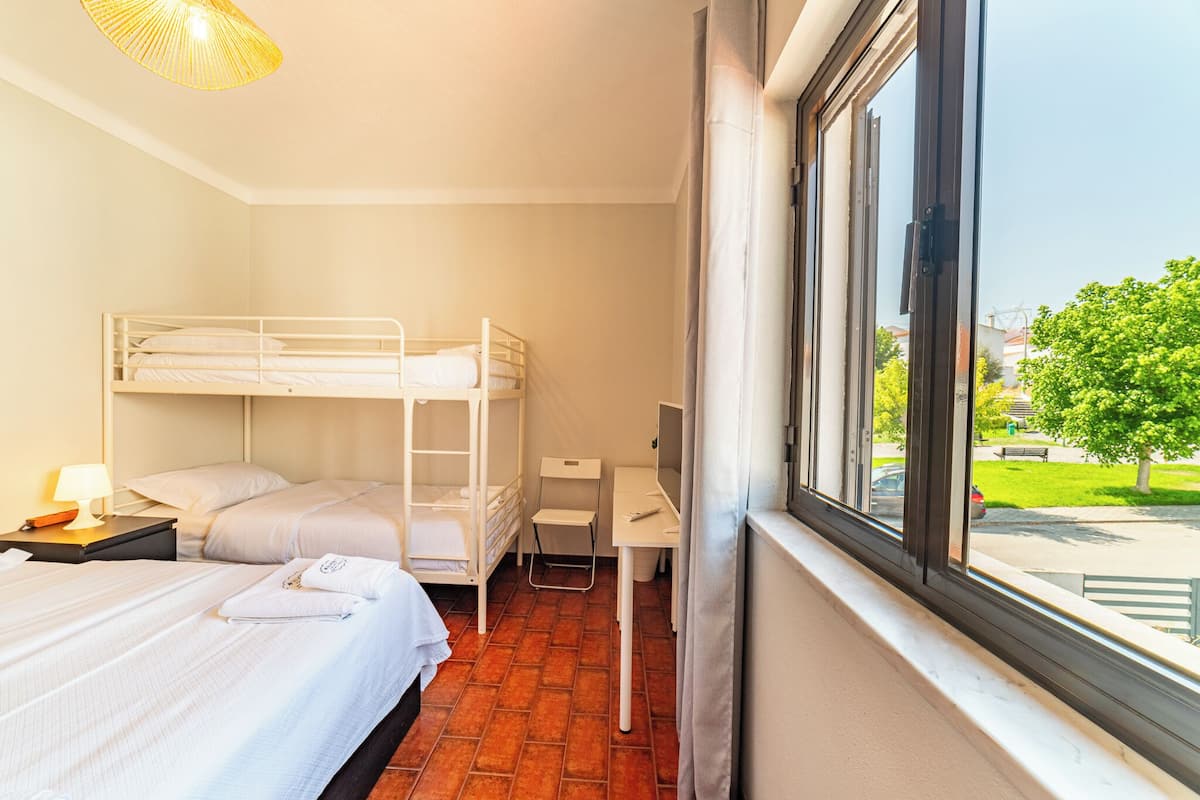 A hotel room with a bunk bed, a desk, and a window with a view of the outside.