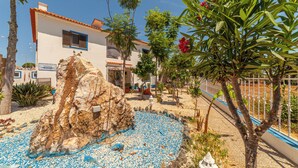 A courtyard with a rock formation, a white building with blue trim, and a fenced area with trees and plants. - 4Ever Palace Design & Nature (Alcacer do Sal)