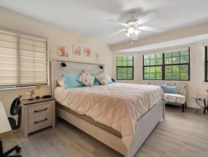 Relax in this serene bedroom with a large bed, two nightstands, and a ceiling fan. Enjoy the view from the window overlooking lush greenery.