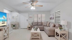 En moderne stue med en beige sofa, et sofabord, et fjernsyn og en loftventilator.