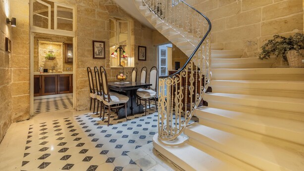 Un magnifique escalier orné de rampes en métal ouvragé, une salle à manger avec un sol à motifs et des murs en pierre.