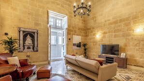 Un vaste salon avec un canapé beige, des fauteuils en cuir et un téléviseur. Un lustre est suspendu au plafond et une statue est fixée au mur.