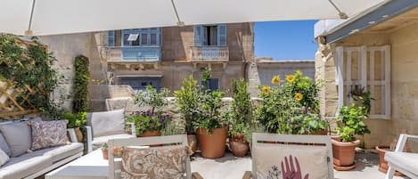 Un espace extérieur aménagé avec des meubles blancs, des plantes en pot et un auvent blanc.