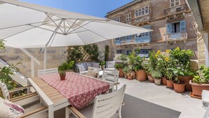 Une terrasse extérieure avec une table et des chaises, un parasol blanc et des plantes en pot.