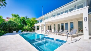 A modern pool area with a clear blue pool, lounge chairs, and a glass-enclosed patio. - Luxurious Oceanfront Villa El Oceano with Ocean views (Grand Harbour)