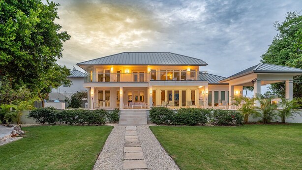 A two-story house with a covered porch, a gravel pathway leading to the entrance, and a well-maintained lawn. - Luxurious Oceanfront Villa El Oceano with Ocean views (Grand Harbour)