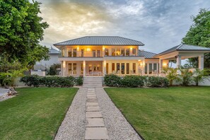 A two-story house with a covered porch, a gravel pathway leading to the entrance, and a well-maintained lawn. - Luxurious Oceanfront Villa El Oceano with Ocean views (Grand Harbour)