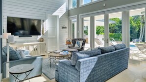 A spacious living room with a large TV, comfortable seating, and a view of the outdoor pool area. - Luxurious Oceanfront Villa El Oceano with Ocean views (Grand Harbour)
