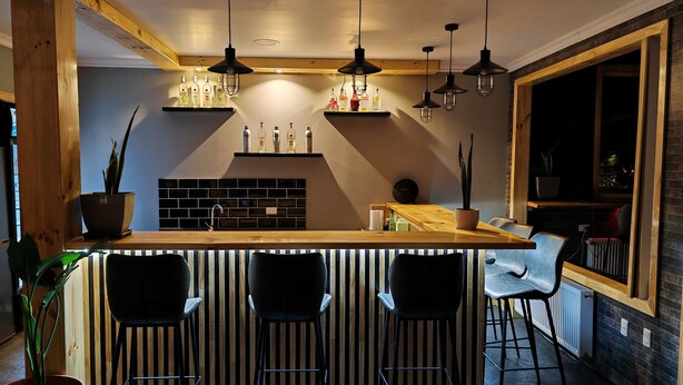A modern kitchen with a wooden island, black bar stools, and pendant lighting. - SHEUEN PATAGONIA (Natales)