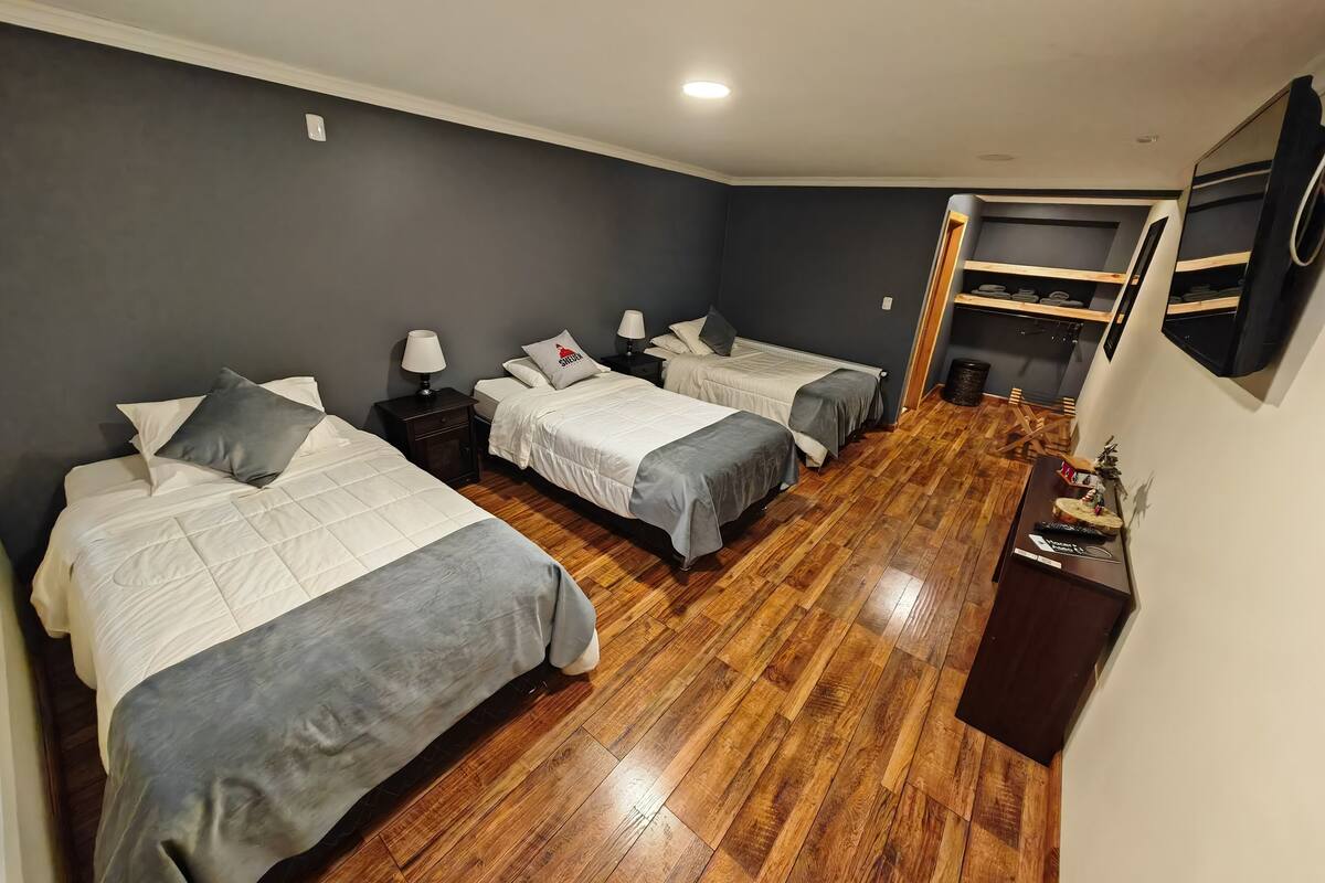 A room with three beds, wooden flooring, and a TV mounted on the wall.