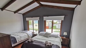 A bedroom with two beds, wooden beams, a window with a view, and a red rug. - SHEUEN PATAGONIA (Natales)
