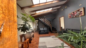 A modern living room with a wooden floor, a black leather sofa, a staircase, and a skylight. - SHEUEN PATAGONIA (Natales)