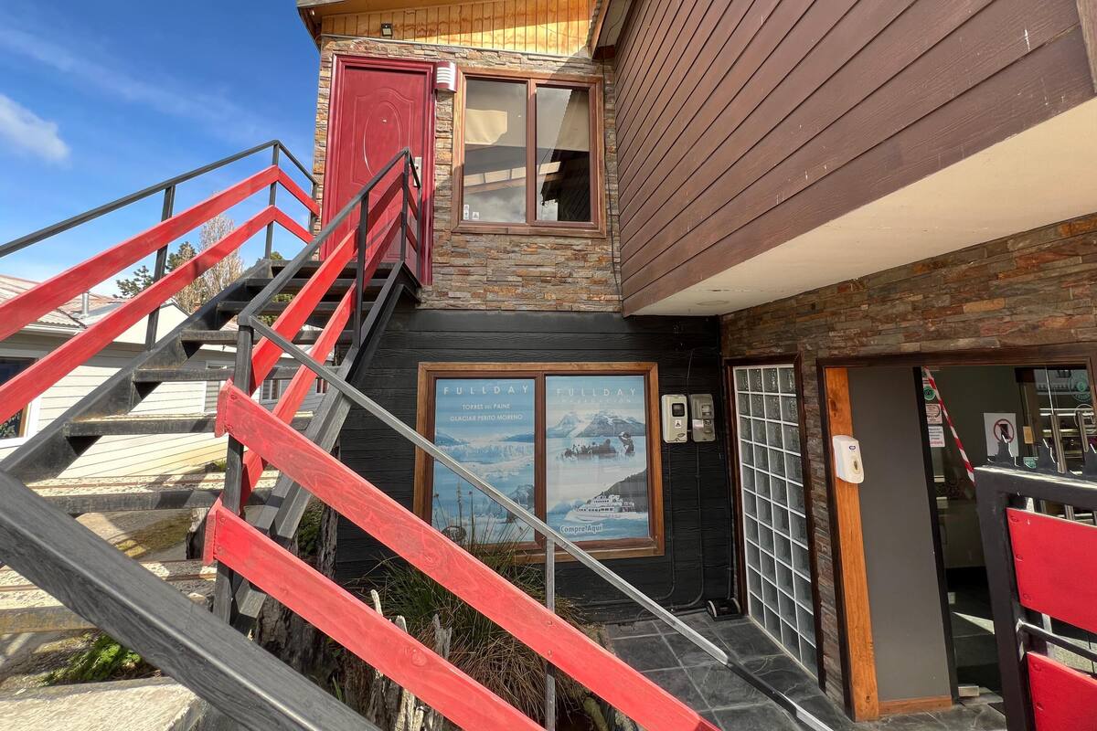A building with a wooden exterior, a red door, and a staircase with red railings leading to a second floor.