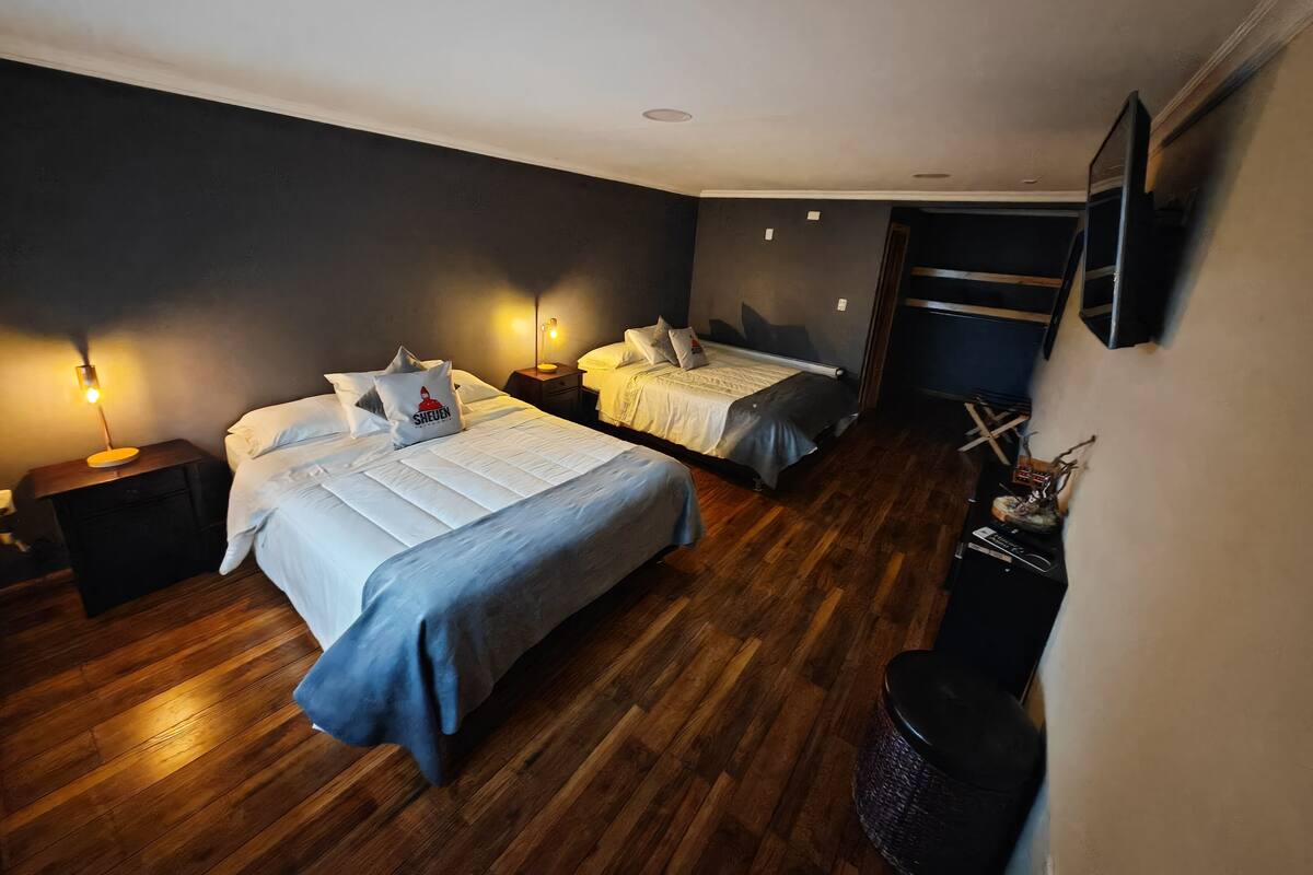 A bedroom with two beds, wooden flooring, bedside lamps, and a mounted TV.