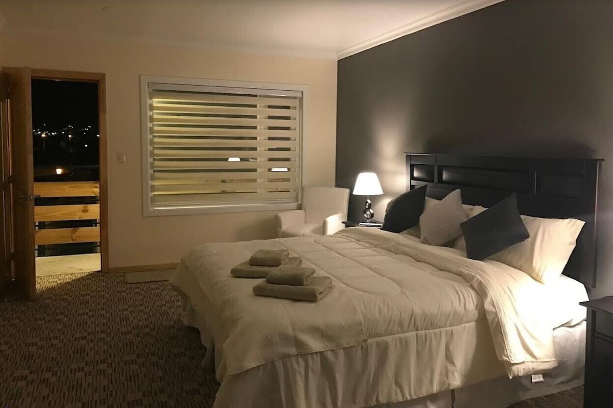 A bedroom with a bed, bedside tables, a lamp, and a window with blinds.