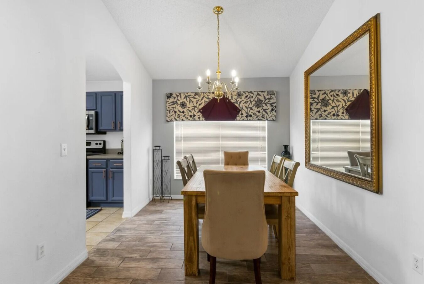 A dining area with a wooden table and chairs, a chandelier, and a large mirror on the wall.