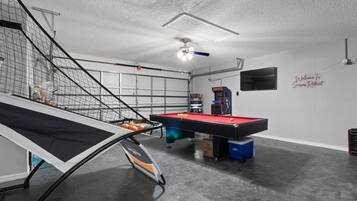 A billiards room with a pool table, a foosball table, and a ping pong table.