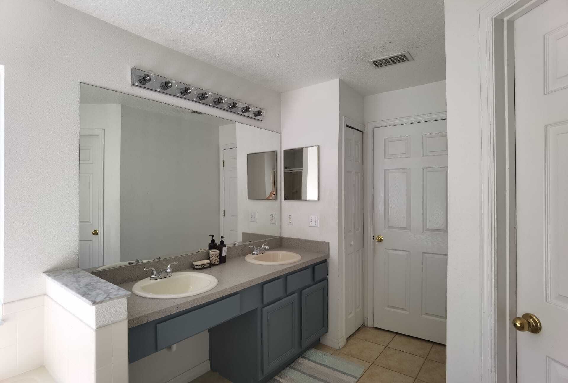 Une salle de bain avec deux lavabos, un grand miroir et une porte.