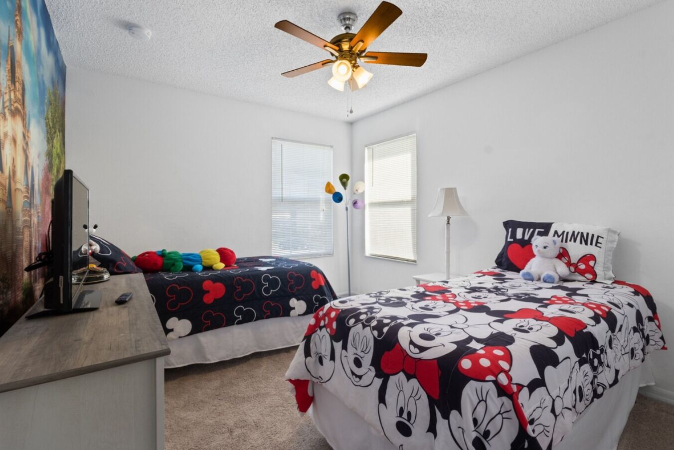 A bedroom with two beds, a ceiling fan, a TV, and a painting on the wall.