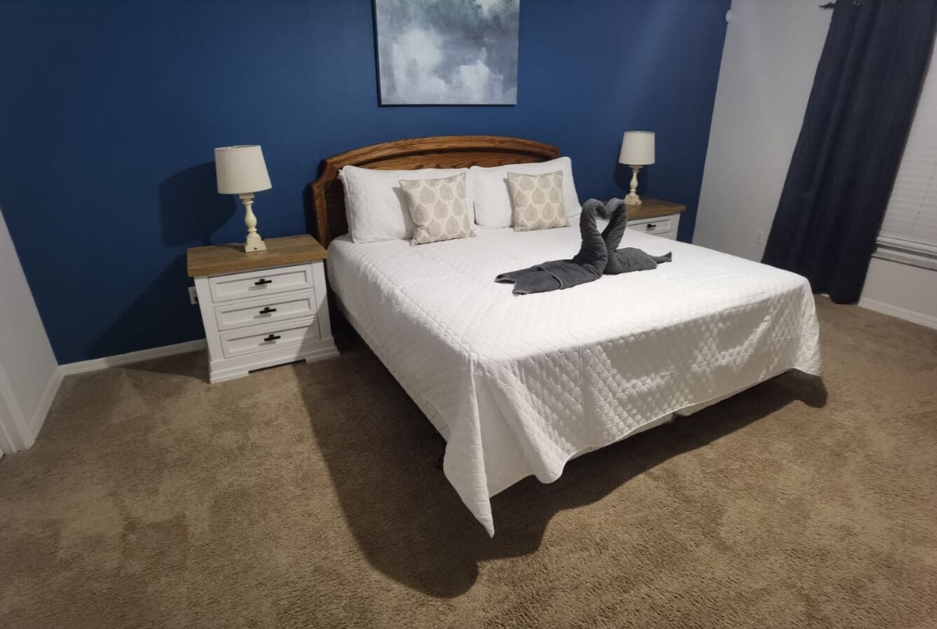 A bedroom with a large bed, two bedside tables, a wooden headboard, and a blue accent wall.