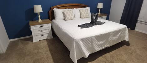 A bedroom with a large bed, two bedside tables, a wooden headboard, and a blue accent wall.