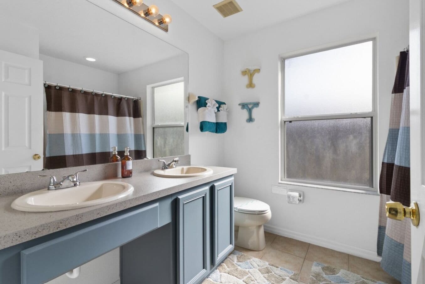 A bathroom with two sinks, a toilet, a shower curtain, and a window.