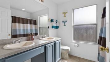 A bathroom with two sinks, a toilet, a shower curtain, and a window.