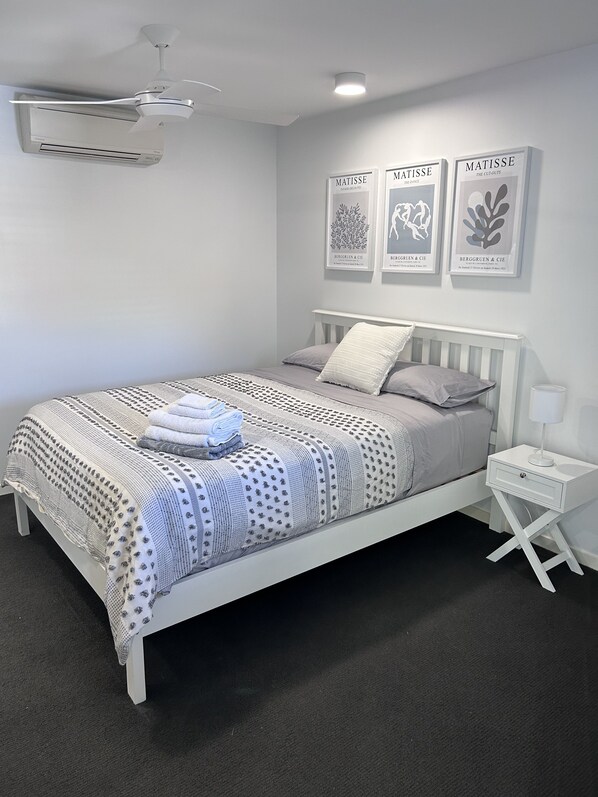 A modern bedroom with a white bed, grey bedding, and a white nightstand with a lamp.