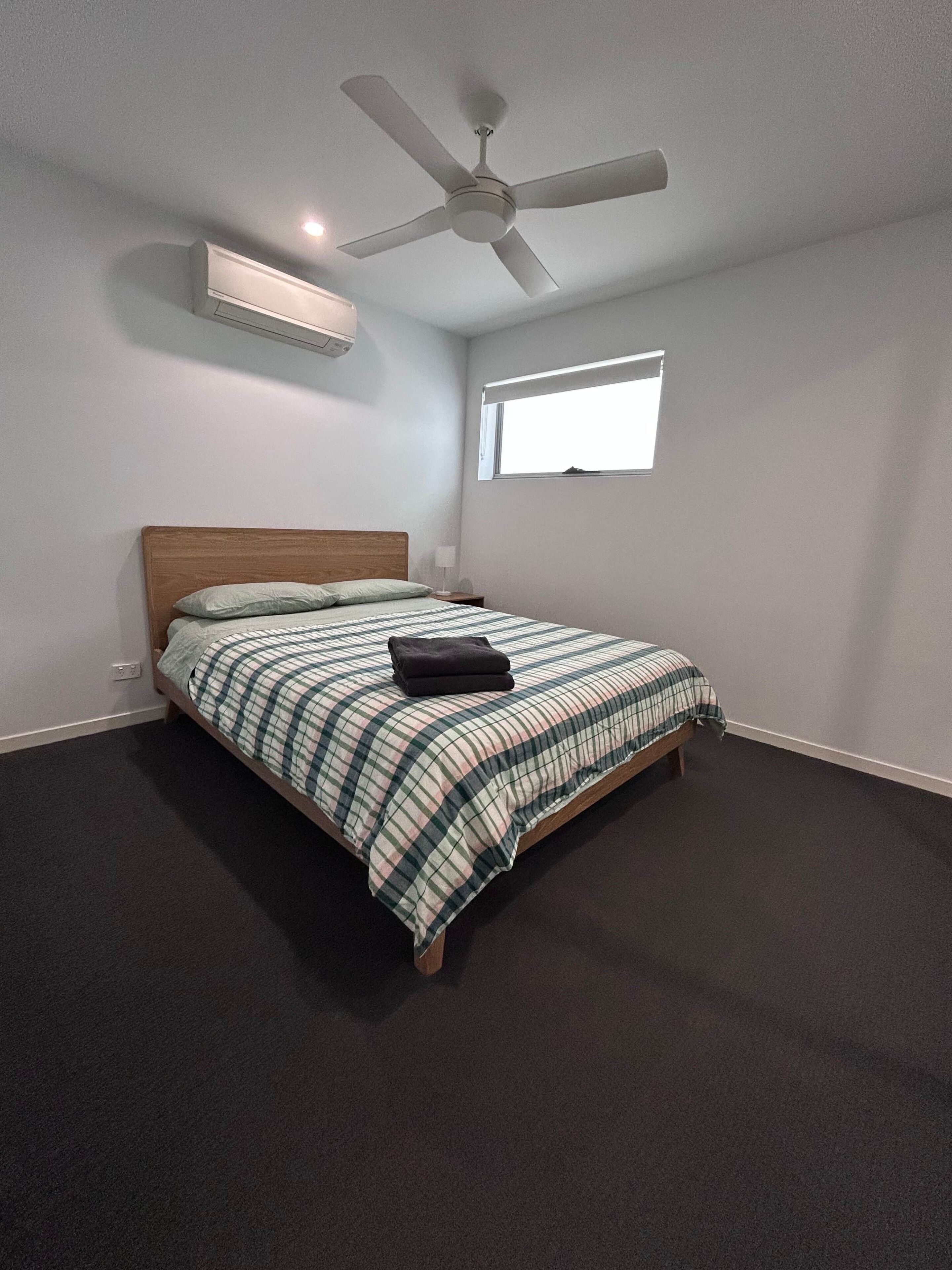 Een slaapkamer met een bed, een plafondventilator, een raam en een wandairconditioner.