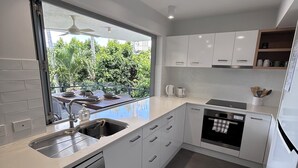 A modern kitchen with white cabinetry, a built-in dishwasher, and a window overlooking a balcony with greenery. - Great size close to the action (Manly)
