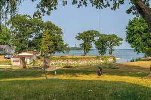 Un espace verdoyant avec un hamac, des arbres, un petit abri et une étendue d’eau en arrière-plan.
