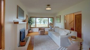 Un salón amplio con un ventanal grande, una chimenea, un sofá y una mesita.