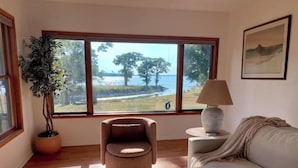 Una habitación con un ventanal grande, una planta en maceta, un sillón redondo, un sofá blanco y una lámpara.