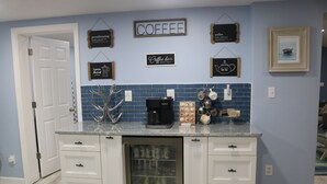 Cucina con mobili bianchi, macchina da caffè e frigorifero. Sono presenti insegne a parete e una cornice con un'immagine.
