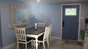 Un'area pranzo con un tavolo in legno e sedie bianche, uno specchio decorativo e una porta blu con una finestra.