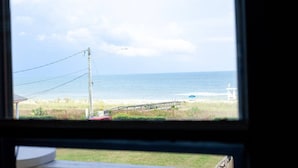 Blick auf einen Strand aus einem Fenster, einschließlich eines Holzstegs, eines Rettungsturms und eines klaren Himmels.