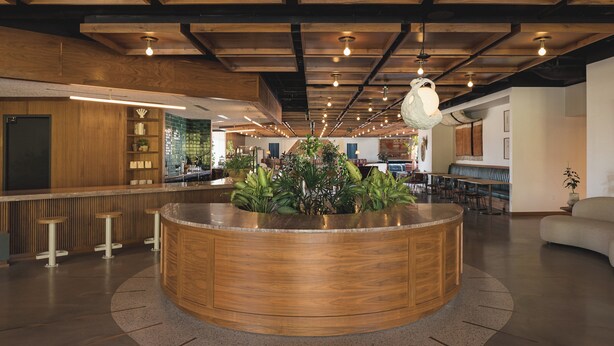 Un vestíbulo amplio con un mostrador de recepción de madera en el centro, zona de bar, asientos e iluminación colgante.