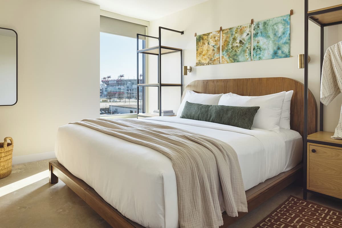 A modern bedroom with a large bed, a wooden headboard, a view of the city, and abstract art on the wall.