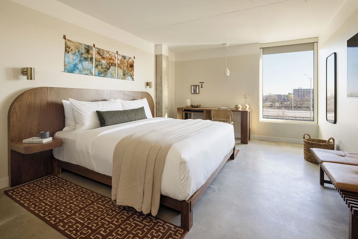 A modern hotel room with a large bed, a desk, and a view of the city.