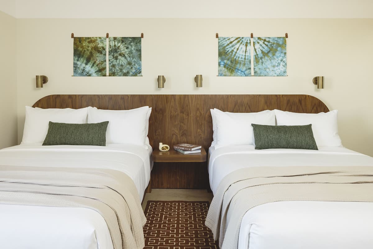 A double room with two beds, a wooden headboard, a nightstand with a book and a vase, and two wall-mounted paintings.